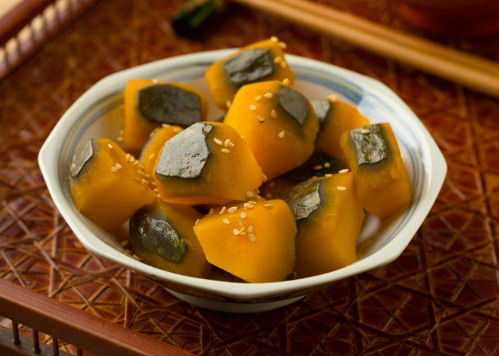 Kabocha pumpkin in a white bowl, garnished with sesame seed.